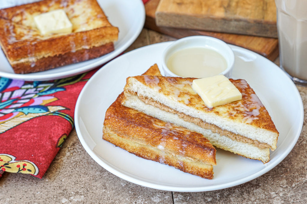 Hong Kong Style French Toast on two white plates drizzled with sweetened condensed milk.