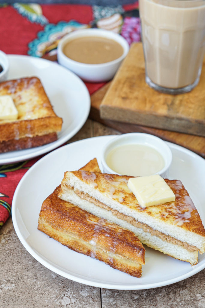 Hong Kong Style French Toast topped with butter and sweetened condensed milk on two white plates with a glass of milk tea.