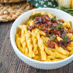 Pumpkin and Cider Macaroni and Cheese in a white bowl with bacon and sage.