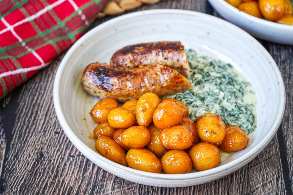 Brunede Kartofler (Danish Browned Potatoes) on a plate with sausage and creamed kale.