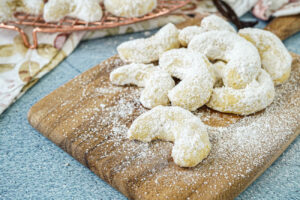 Vanillekipferl (Austrian Vanilla Crescent Cookies) on a wooden board with powdered sugar.