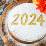 Vasilopita (Greek New Year's Cake) on a wooden board covered in powdered sugar with the stencil 2024 over the top.
