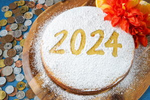Vasilopita (Greek New Year's Cake) on a wooden board covered in powdered sugar with the stencil 2024 over the top.