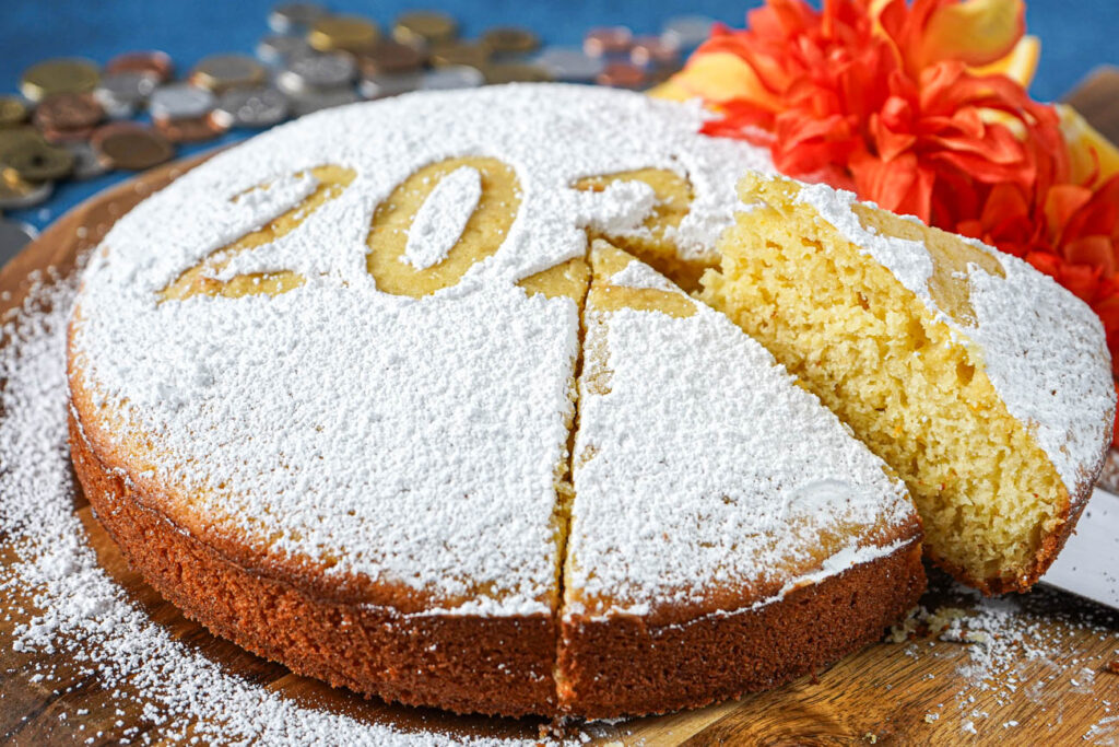 Vasilopita (Greek New Year's Cake) with a slice lifted out and orange flowers and coins in the background.