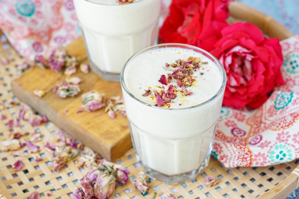 Badam Paal (Indian Almond Milk) in a clear glass topped with saffron, cardamom, and dried rose petals.