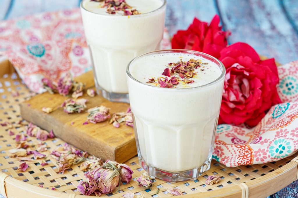 Badam Paal (Indian Almond Milk) in two clear glasses topped with saffron, ground cardamom, and dried rose petals.
