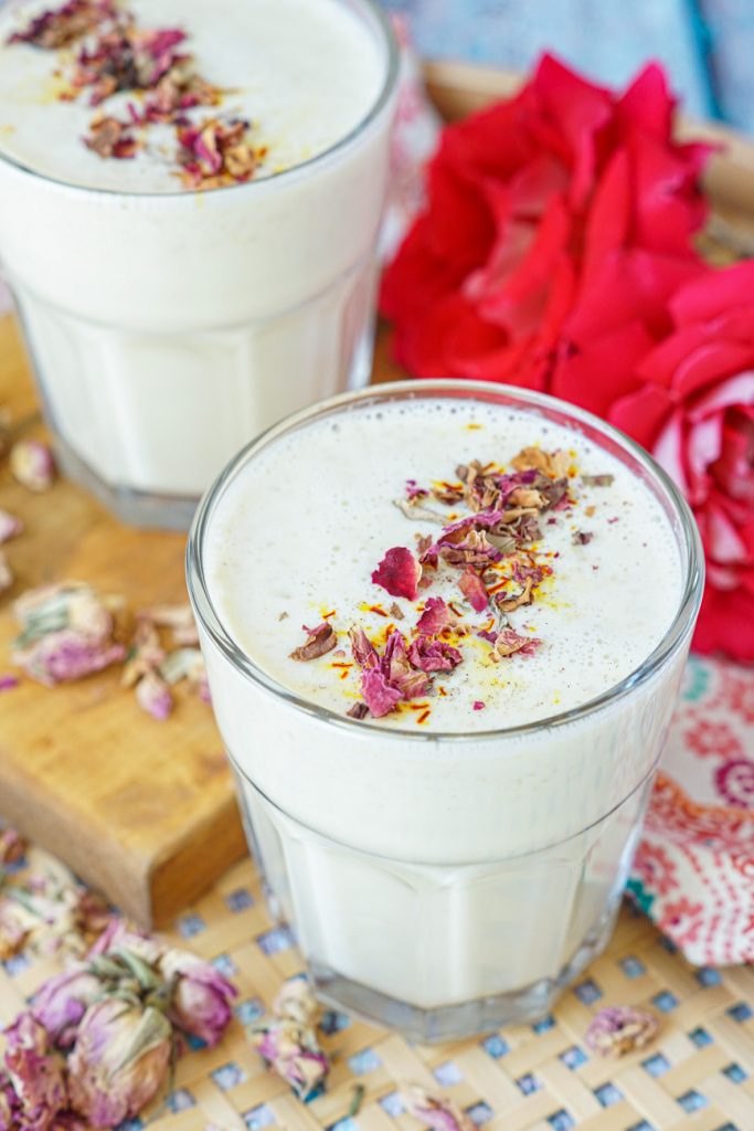Close up of Badam Paal (Indian Almond Milk) in a clear glass with roses in the background.