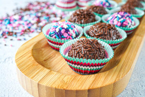 Nine Brigadeiros (Brazilian Fudge Balls) on a wooden board with sprinkles in the background.