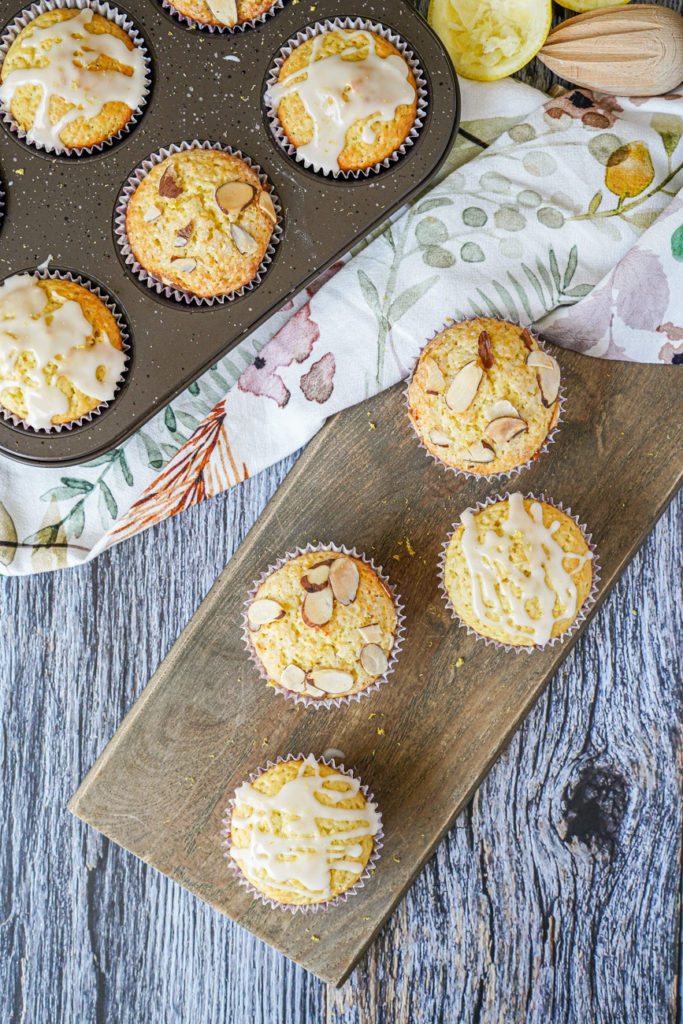 Aerial view of four Lemon Ricotta Muffins on a wooden board with more in a muffin tin.