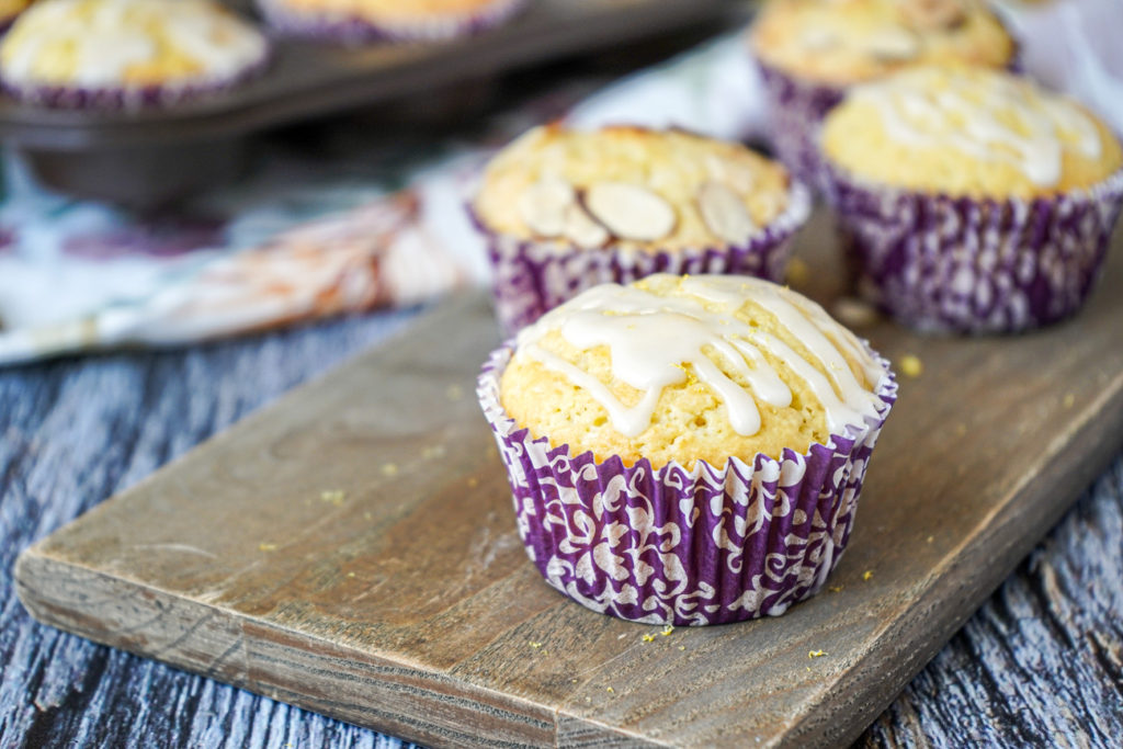 Four Lemon Ricotta Muffins with purple liners on a wooden board.