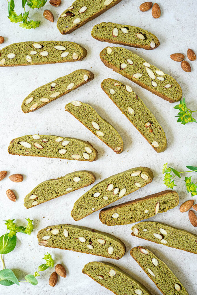 Aerial view of Matcha Almond Biscotti next to almonds and green flowers.
