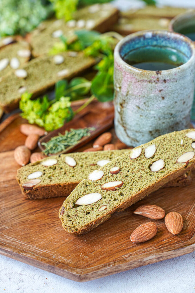 Close up of two Matcha Almond Biscotti next to a tea cup with more biscotti in the background.