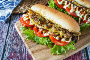 Roti John (Omelette Sandwich) on a wooden board with tomatoes and lettuce.
