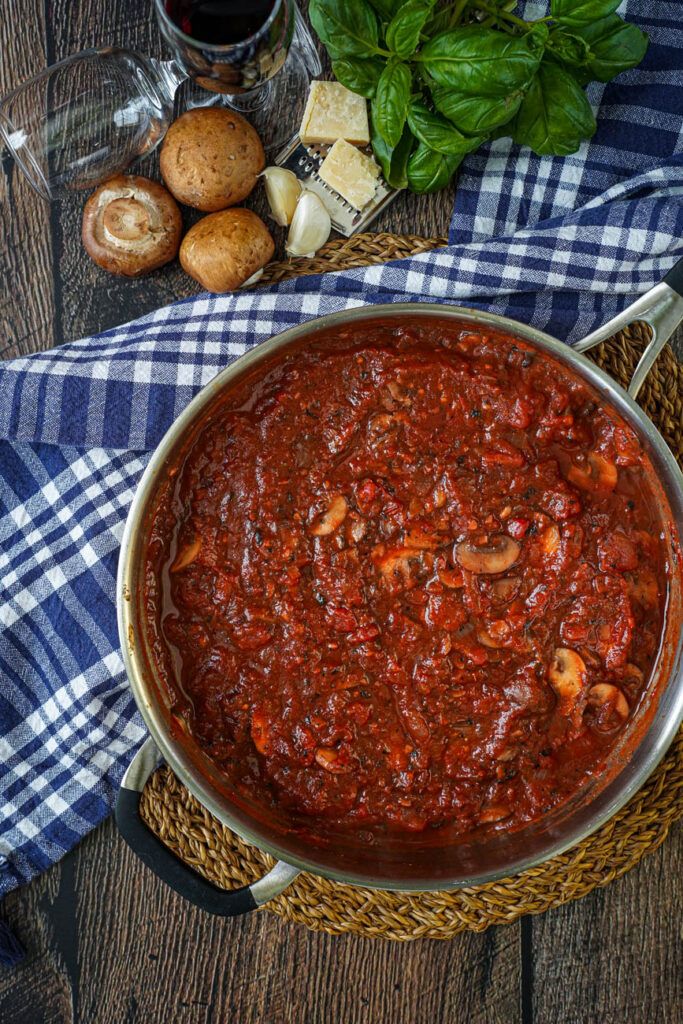 Aerial view of Mushroom Tomato Sauce in a steel pan next to mushrooms, garlic, cheese, and basil.