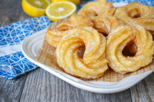 A pile of Spritzkuchen (German Crullers) on a white platter with lemons in the background.