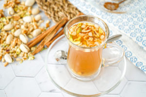 Aynar (Lebanese Spiced Tea) in a clear glass with chopped nuts.