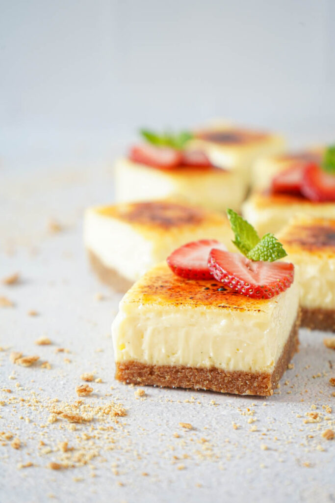 Side view of Creme Brulee Cheesecake Bars topped with strawberries and mint.