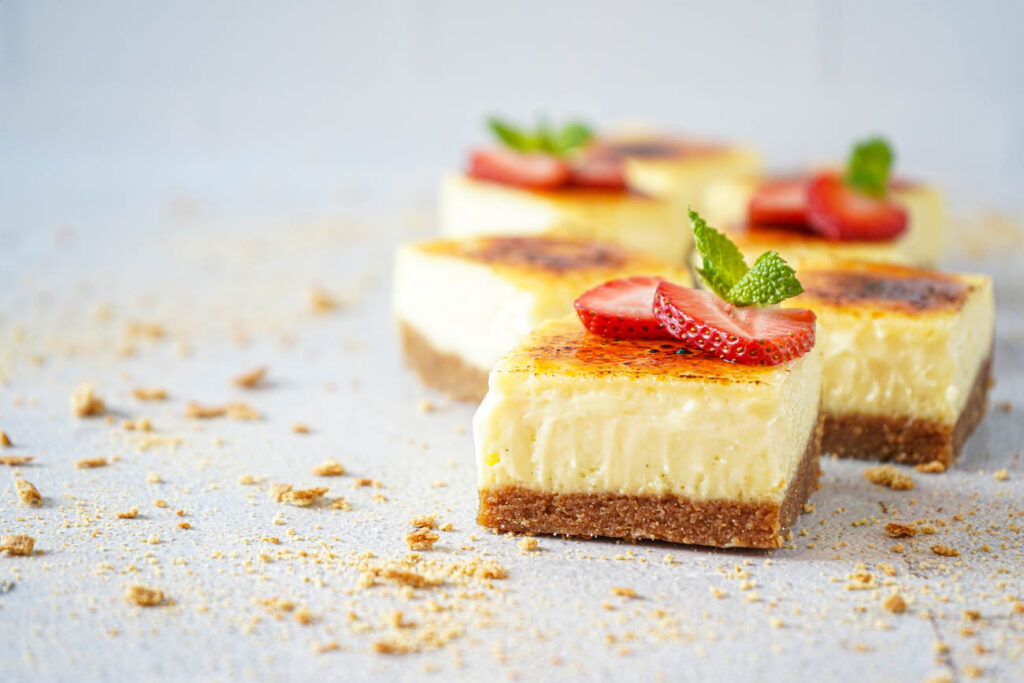Creme Brulee Cheesecake Bars topped with strawberry slices and fresh mint.