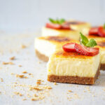 Creme Brulee Cheesecake Bars topped with strawberry slices and mint sprigs.