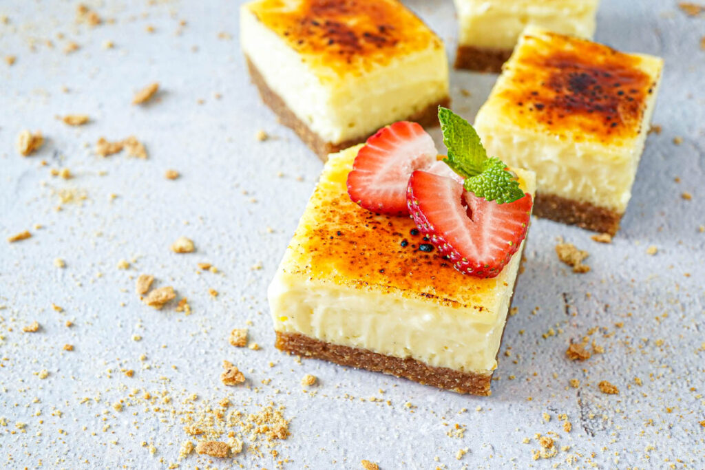Close up of Creme Brulee Cheesecake Bars with one topped with strawberry slices.