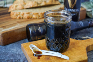 Guinness Reduction Dipping Sauce in a jar in front of Guinness bottles and brown bread.