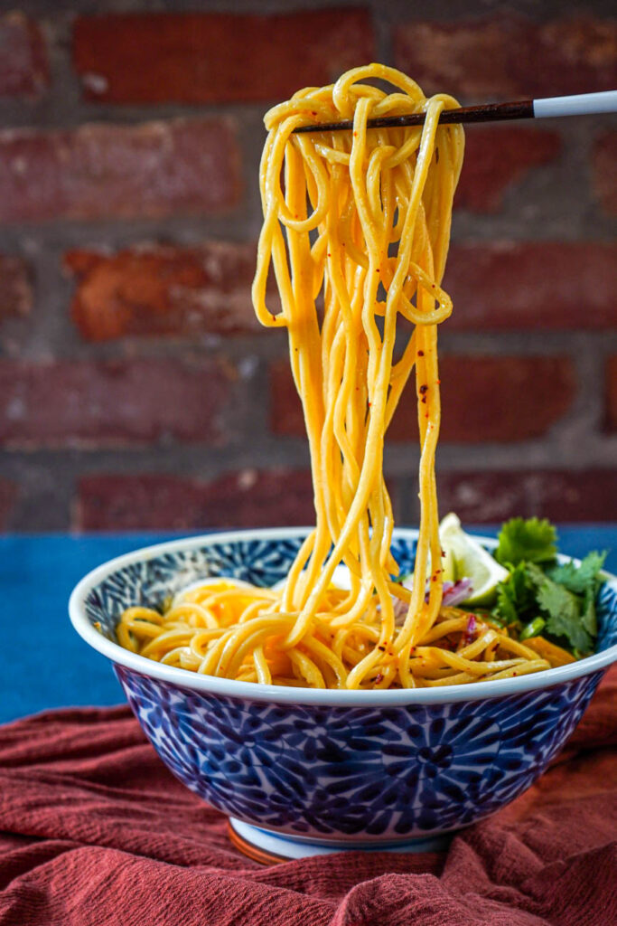 Chopsticks holding up noodles over a bowl.