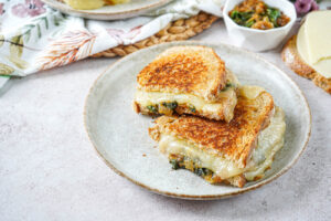 Caramelized Onion and Spinach Grilled Cheese sandwich cut in half on a plate with the cheese oozing out the sides.