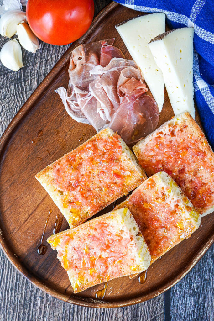 Aerial view of Pa amb Tomàquet (Catalan Bread with Tomato) on a board with ham and cheese.