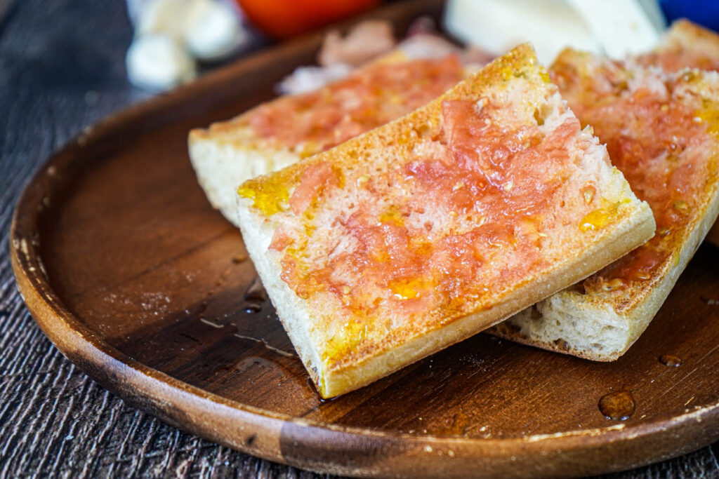 Four slices of Pa amb Tomàquet (Catalan Bread with Tomato) on a wooden board.