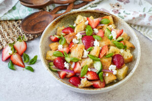 Strawberry Panzanella in a bowl next to a wooden spoon and a wooden fork.