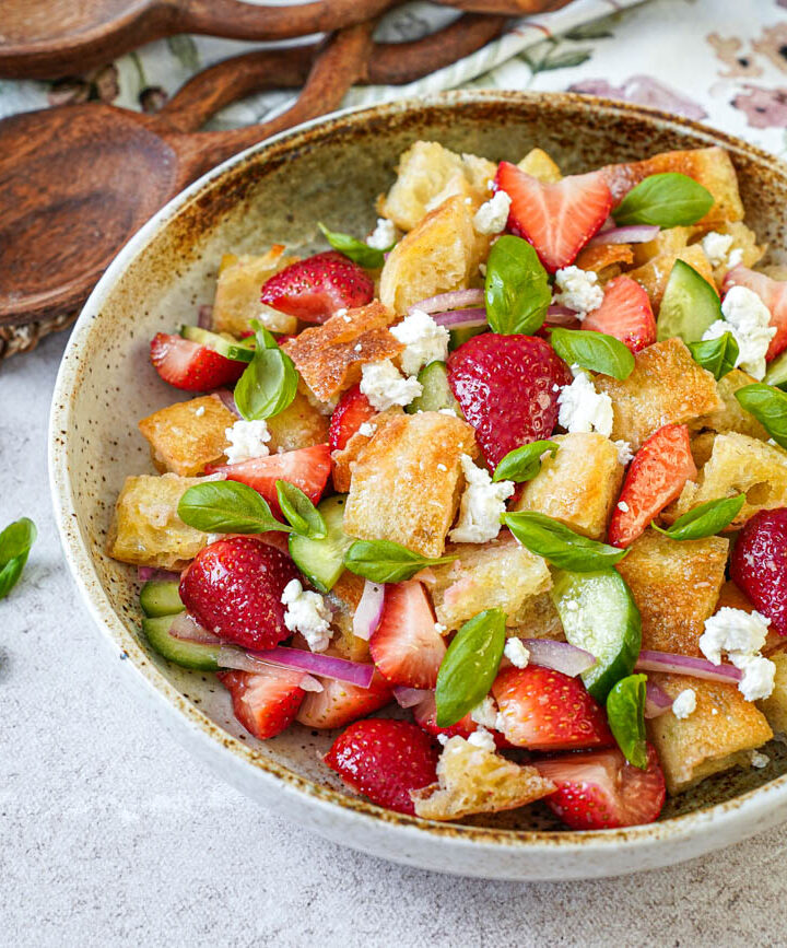 Strawberry Panzanella in a bowl next to a wooden spoon and a wooden fork.