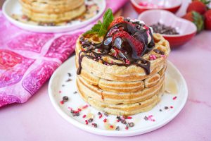 A stack of Strawberry Waffles topped with chocolate sauce, strawberries, and mint.