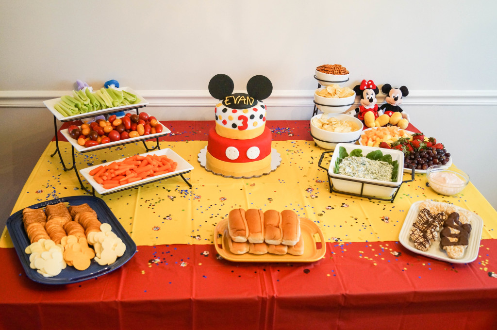 Red and yellow table with food and a Mickey Mouse cake.