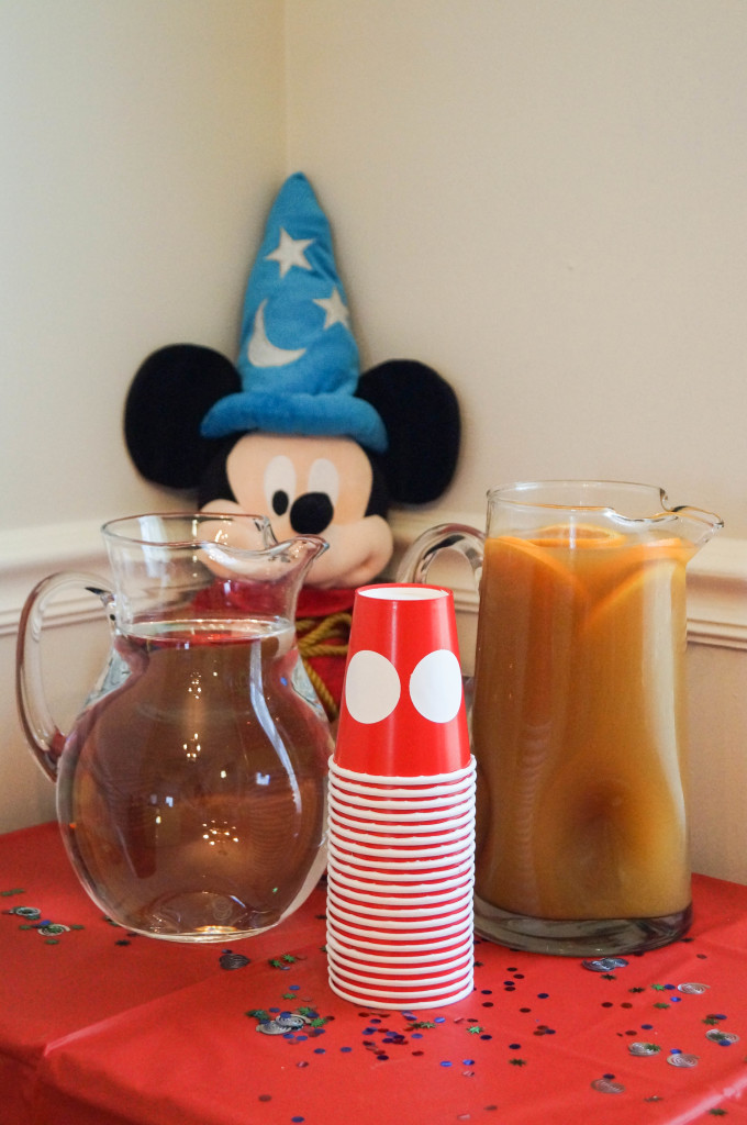 Two glass pitchers filled with drinks next to red paper cups and Mickey Mouse stuffed animal.