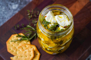 Marinated Goat Cheese in a jar next to crackers, rosemary, and thyme.