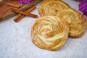 Three Tahinov Hats (Armenian Tahini Bread) spirals next to cinnamon sticks and purple flowers.