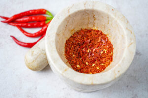 Homemade Chili Flakes in a mortar next to a pestle and red chilies.