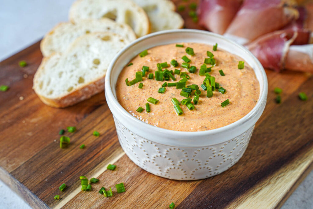Liptauer (Austrian Cheese Spread) in a cream-colored ramekin next to baguette slices and speck.