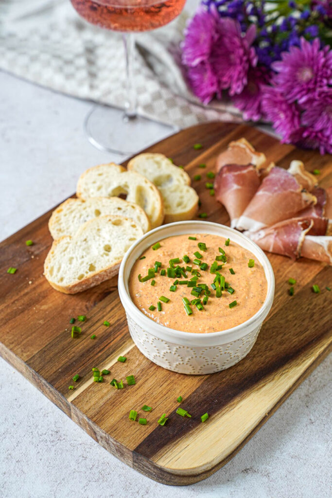 Close up of Liptauer (Austrian Cheese Spread) in a ramekin next to baguette slices and Speck.