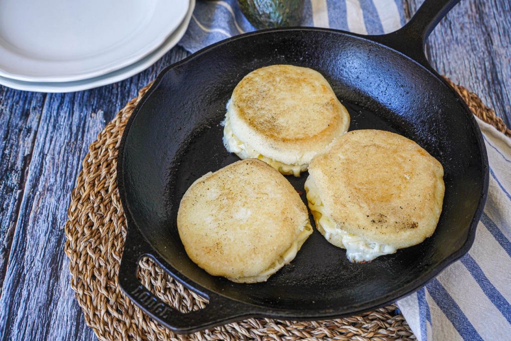 Three Arepas Rellenas de Queso (Cheese Stuffed Corn Cakes) in a cast iron skillet.