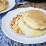 Two Arepas Rellenas de Queso (Cheese Stuffed Corn Cakes) on a plate with scrambled eggs.