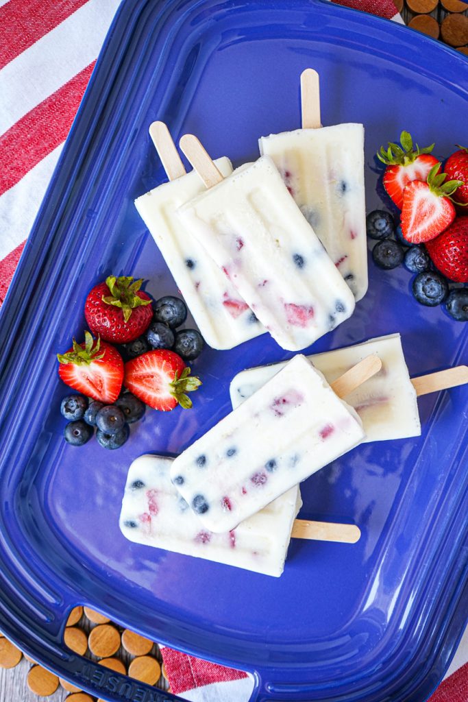 Aerial view of Berry Yogurt Popsicles on a blue platter with fresh berries.