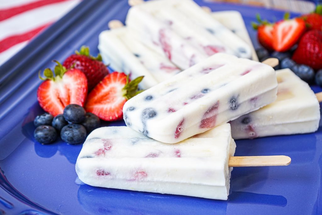 A stack of Berry Yogurt Popsicles on a blue platter next to fresh berries.
