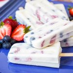 A stack of Six Berry Yogurt Popsicles on a blue platter with fresh berries.