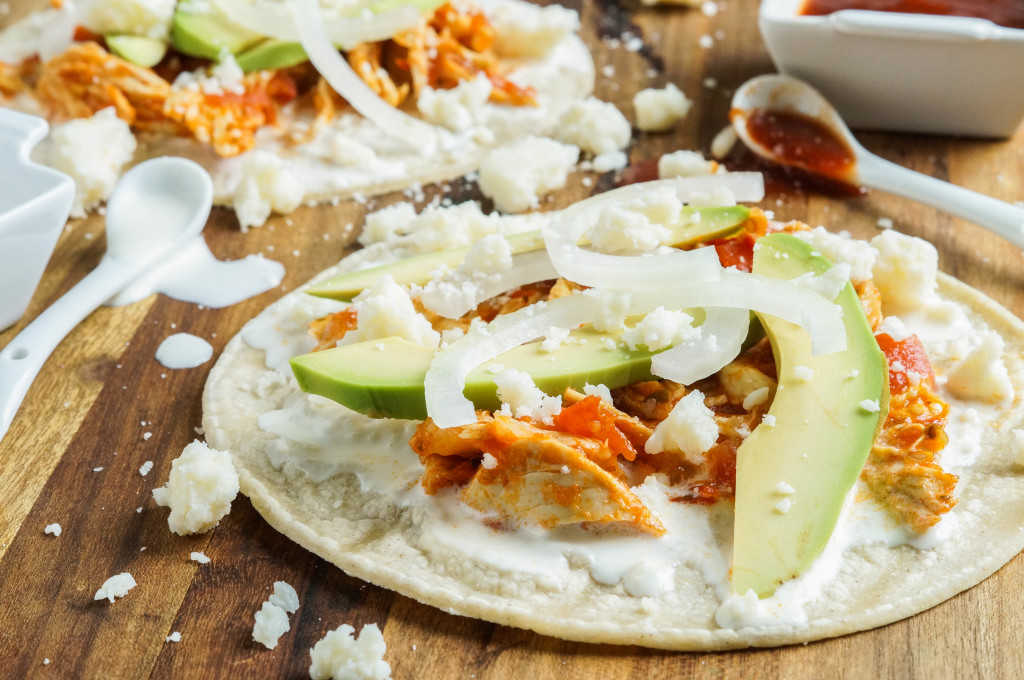 Close up of Chicken Tinga on a tortilla with avocado, sliced onions, and crumbled cheese.