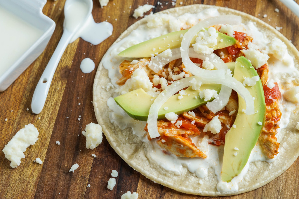 Chicken Tinga on a tortilla with avocado, onion, crumbled cheese, and crema.