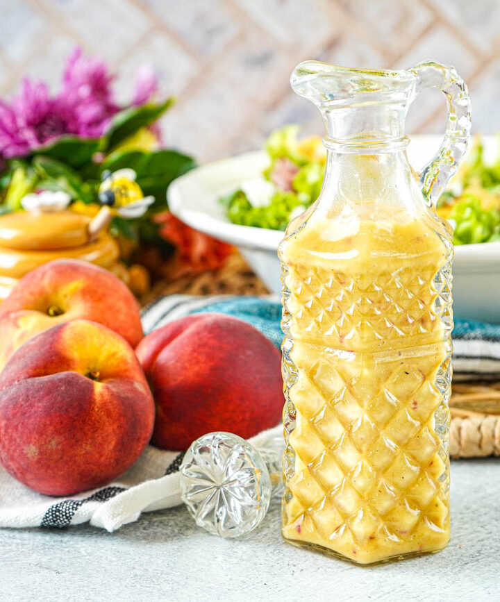 Peach Red Wine Vinaigrette in a crystal tall dressing glass next to fresh peaches and flowers.