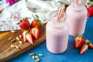 Strawberry Cardamom Lassi in two glasses next to strawberries and cardamom pods.