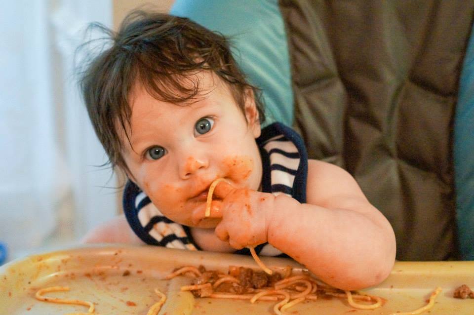 Baby eating spaghetti with her hand.