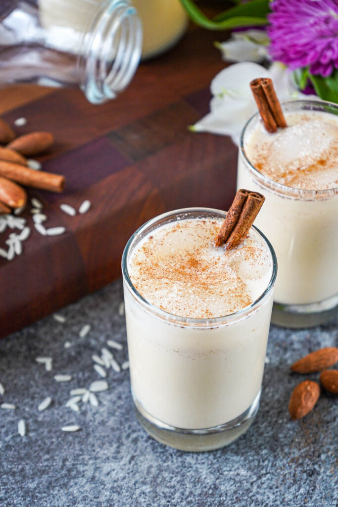 Close up of Horchata in two glasses topped with cinnamon sticks and ground cinnamon.